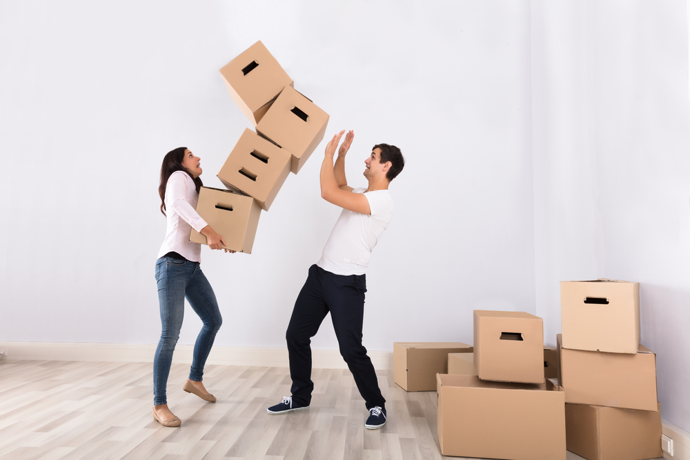 A couple moving boxes but the boxes are falling on the man.