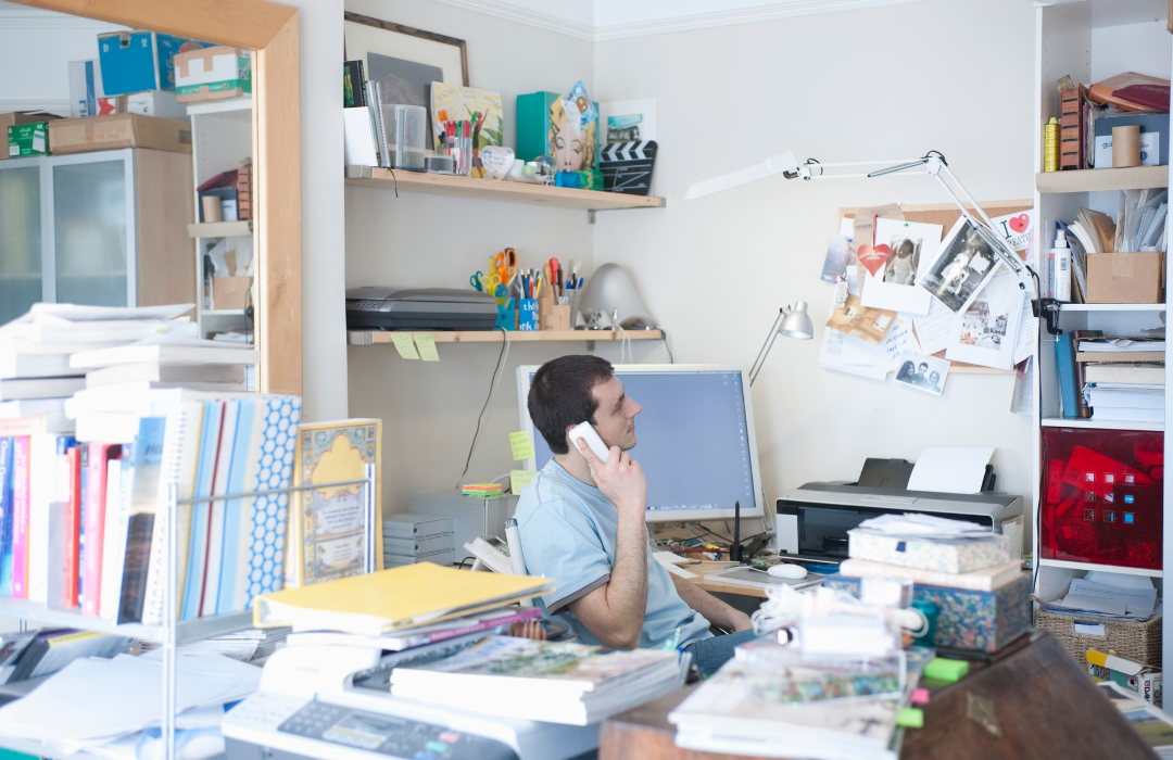 A man sitting in a chair in a very cluttered office.