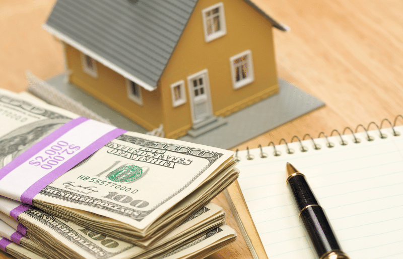 A stack of money and a toy house laying on a table.