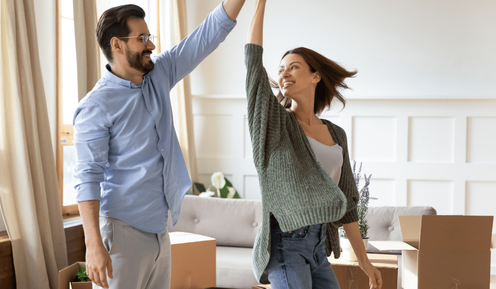 A couple dancing in a living room surrounded by boxes.