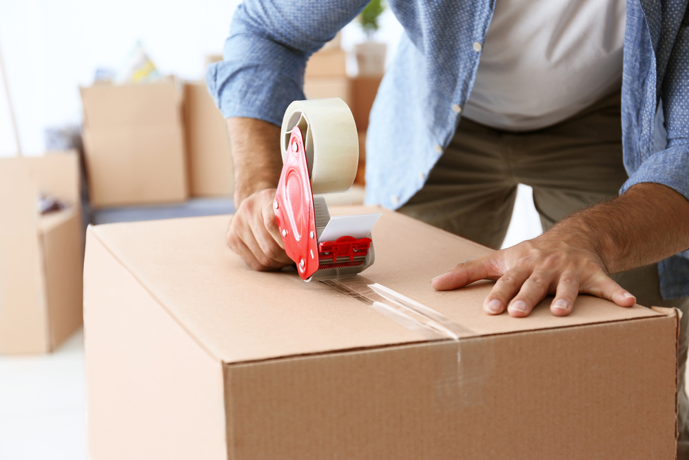 Man taping cardboard box shut.