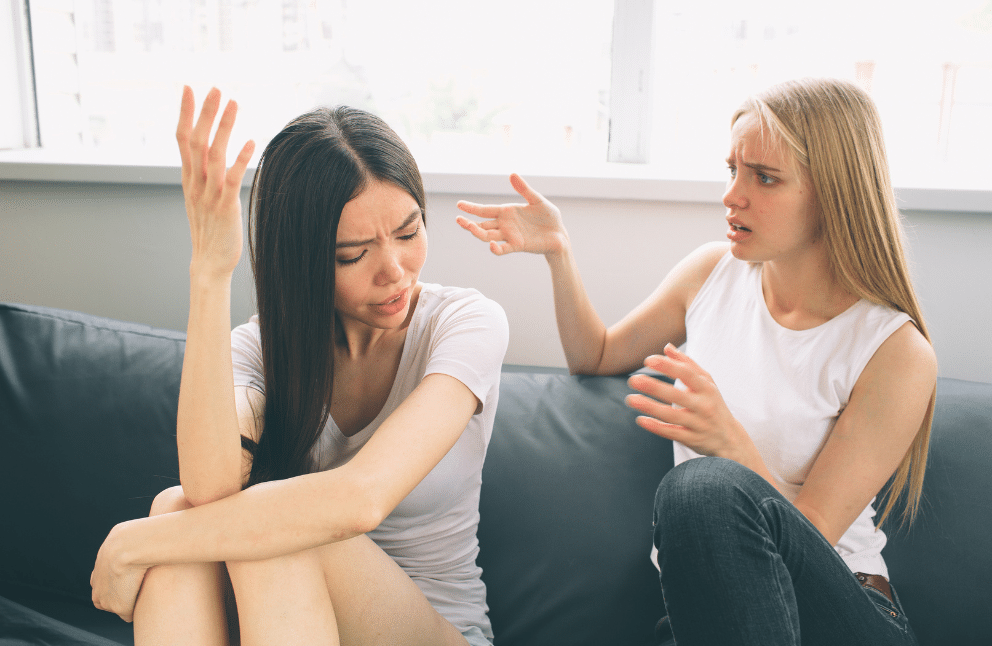 Two girls sitting on a couch having a disagreement.