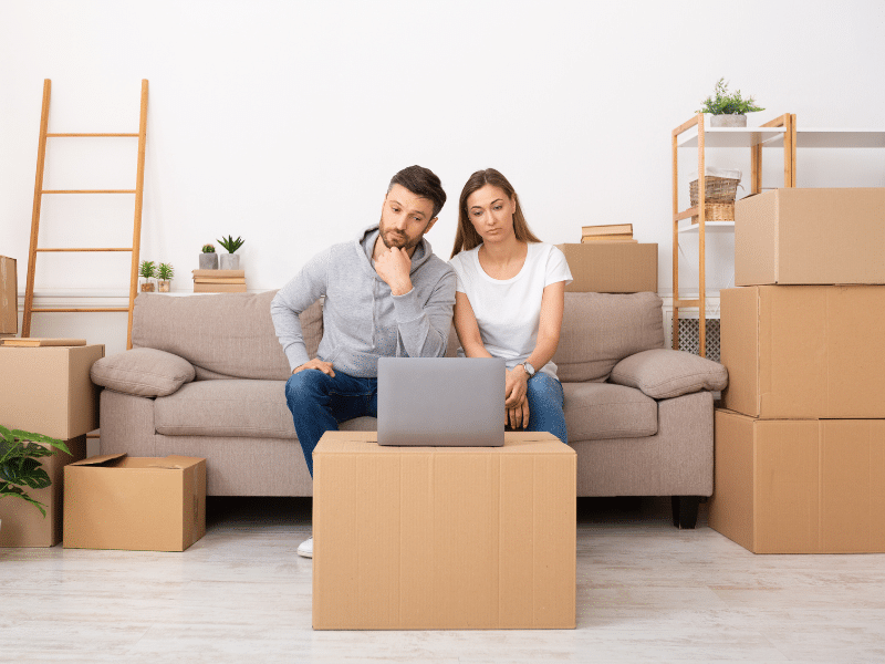 Couple sitting on a couch looking at a computer looking up moving options.