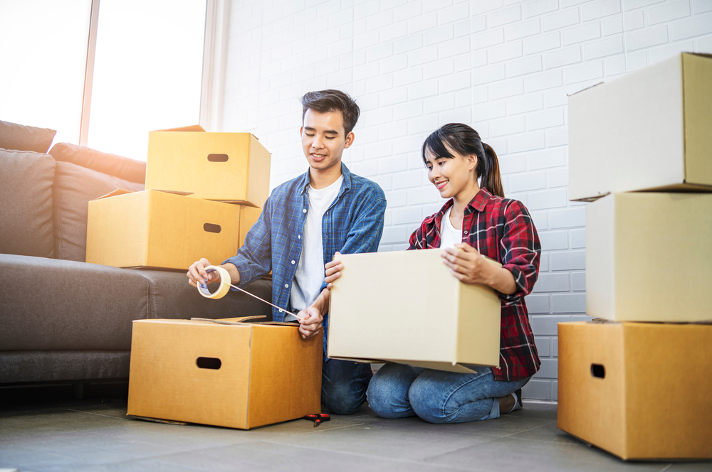 Man and woman taping cardboard boxes closed.