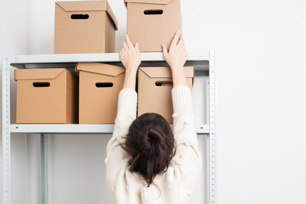 Woman reaching to the top shelf for a cardboard box.