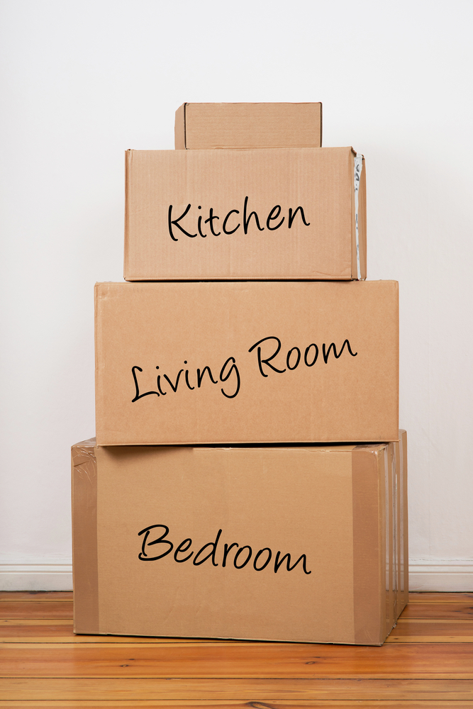 Three cardboard boxes labeled Kitchen, Living room and Bedroom stacked on top of one another.