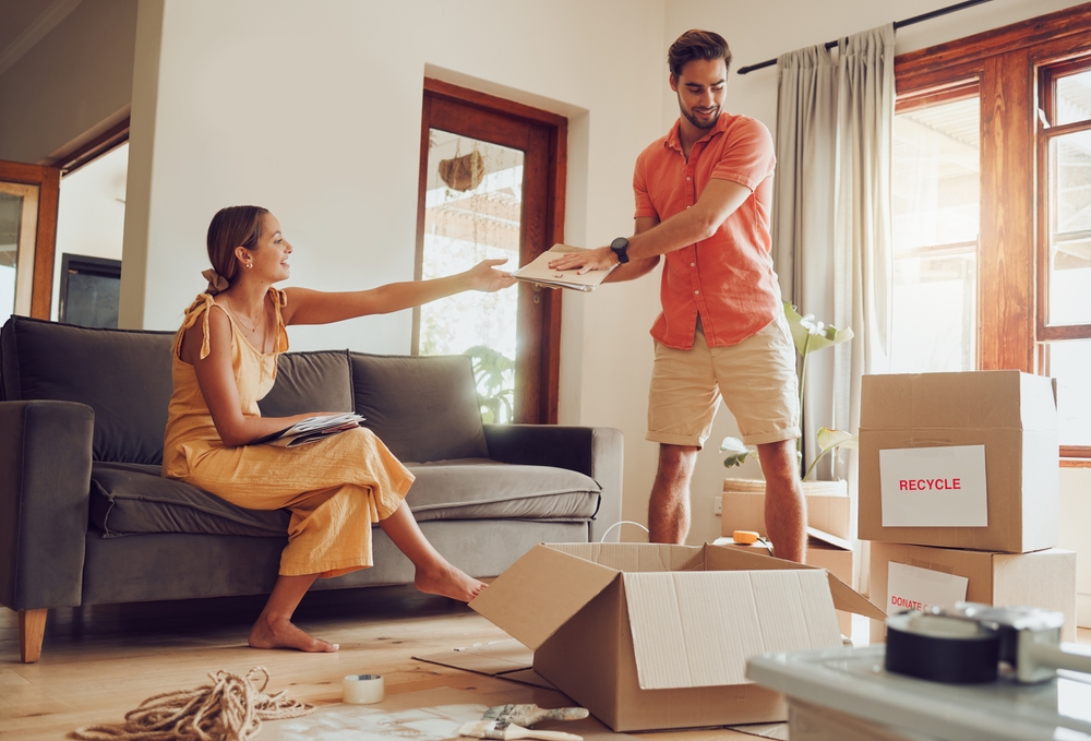 Man handing a stack of papers to a woman sitting on a couch.