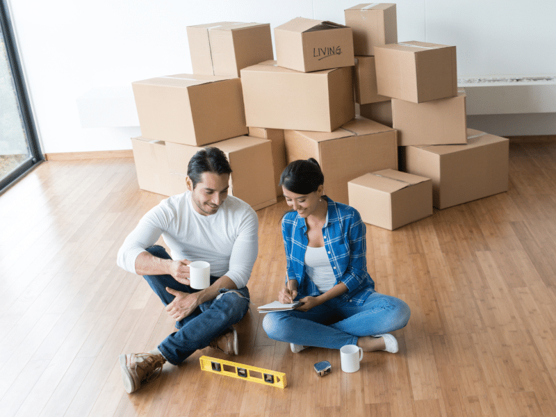 Man and woman sitting on the floor in front of cardboard boxes going over a notebook.