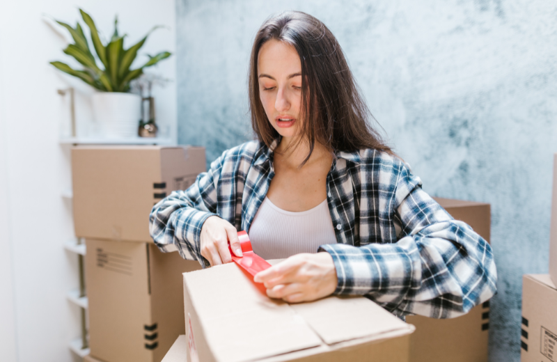 Woman taping a cardboard box shut.