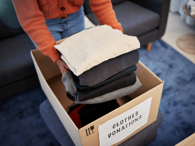 Person putting clothes in a cardboard donation box.