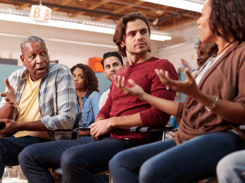 People of various ages in chairs having a discussion.