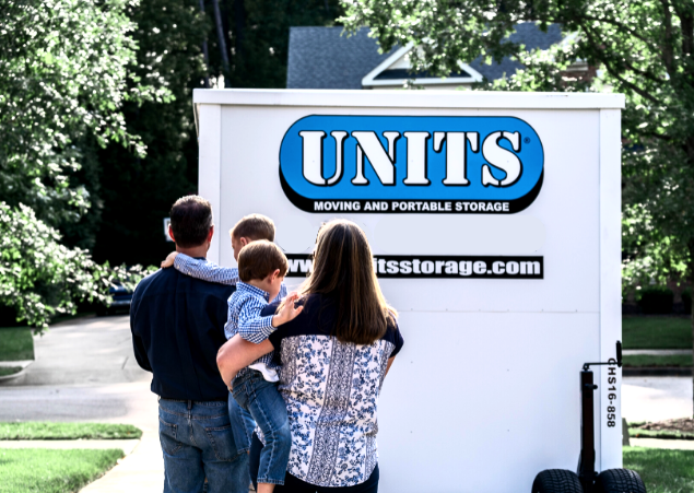 Man and woman each holding a child looking at the back of a UNITS Moving and Portable Storage Container.