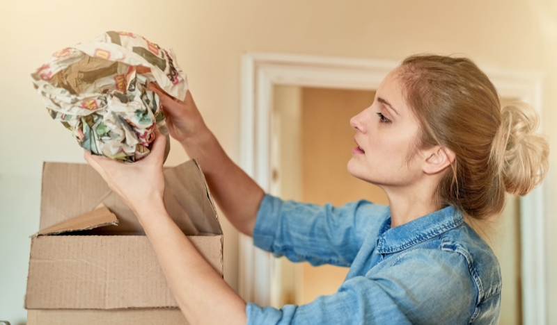 Woman unpacking a wrapped object from a cardboard box.