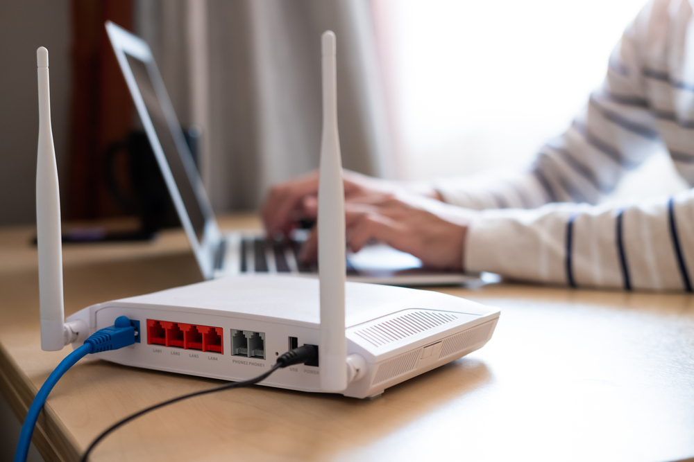 A person looking at their computer with a router next to it.