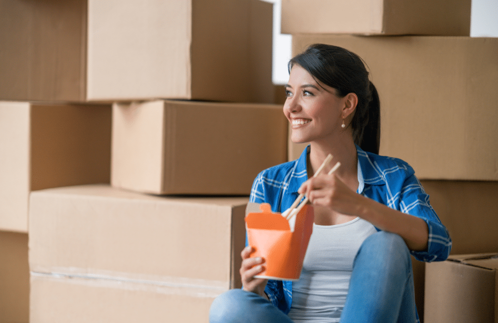 A woman eating Chinese food with chopsticks surrounded by boxes.