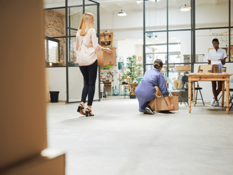 Three people standing in an office moving boxes.