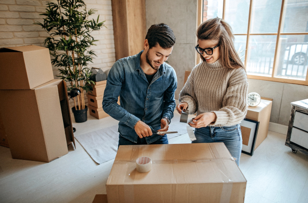 Couple taping a cardboard box shut.