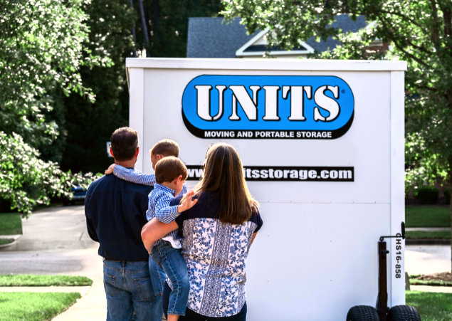 Mother and father each holding one of their young sons, standing in front of their UNITS Moving and Portable Storage container in their driveway.