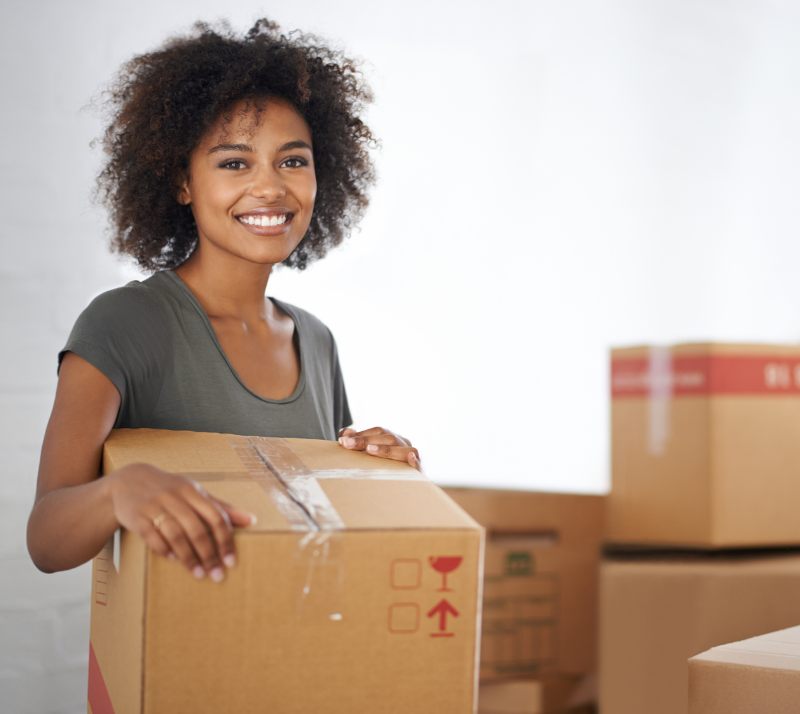 Woman smiling carrying a cardboard box.