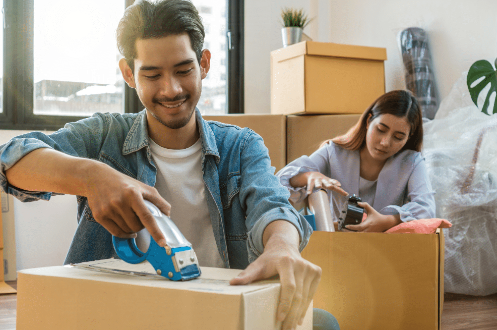 Couple sitting on the floor taping cardboard boxes shut.