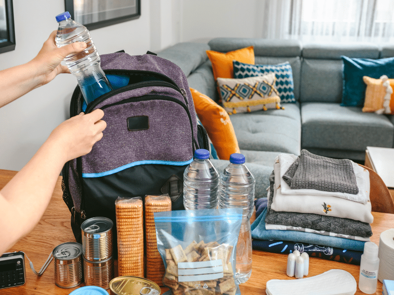 Person packing clothes, food, water bottles and other items into a backpack.