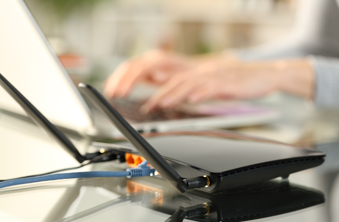 A person typing on their laptop with a wifi router in view.