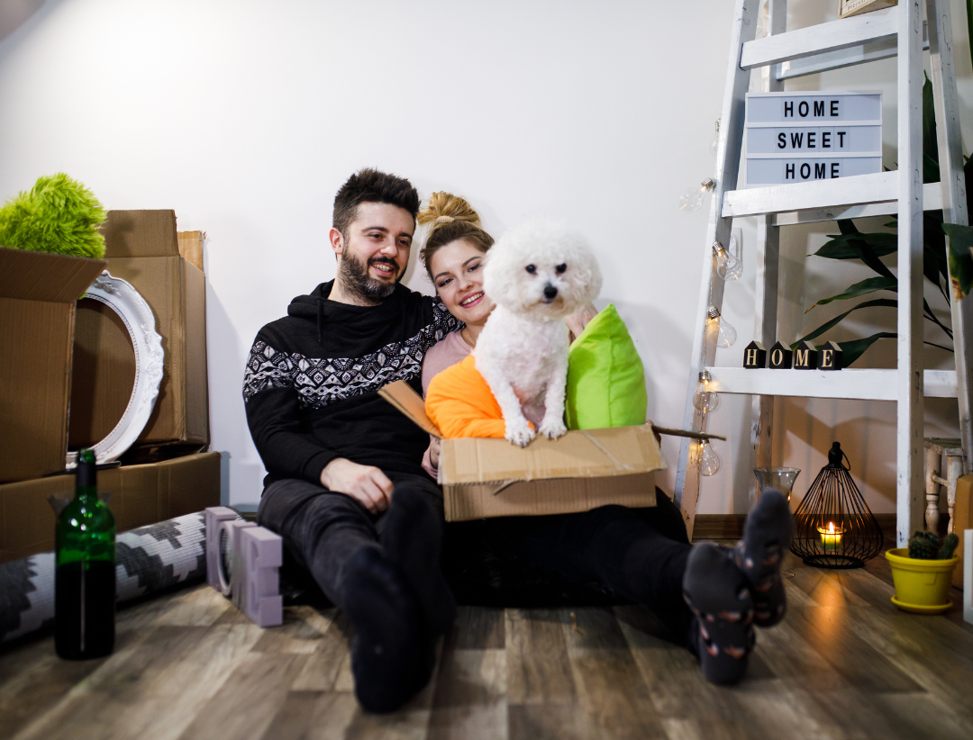 A couple and a dog sitting on the ground surrounded by boxes.