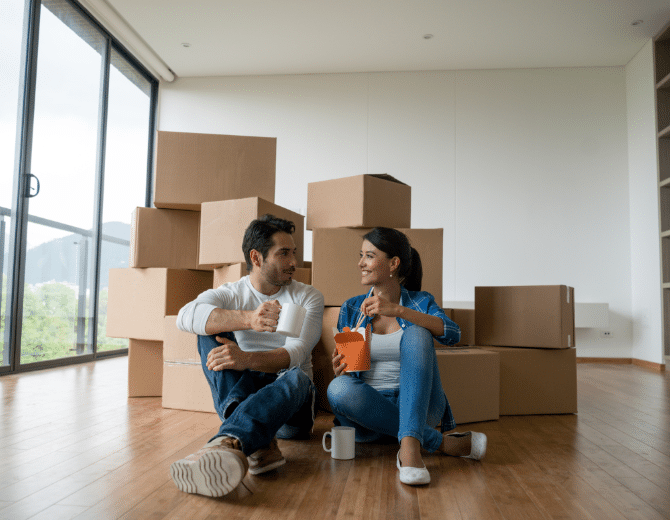 A couple sitting on the ground eating chinese food surrounded by boxes.