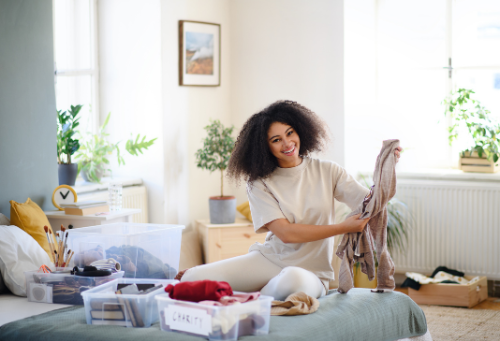 A woman sitting on a bed folding clothes to put in plastic bins.