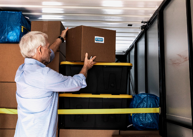 A man packing a box with the units logo on it into a container.