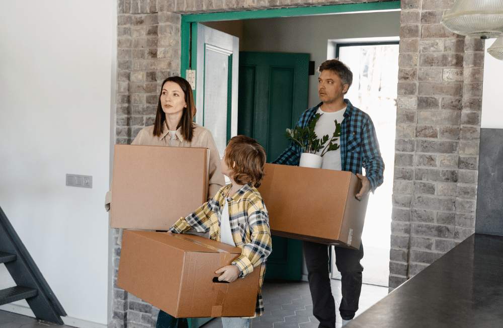 Man, women and their child carrying cardboard boxes into their new house.