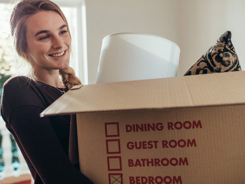 Woman carrying a cardboard box marked Bedroom.