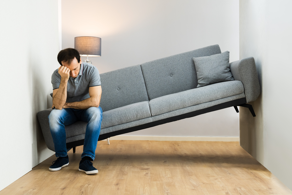 A man having trouble moving a couch through his house.