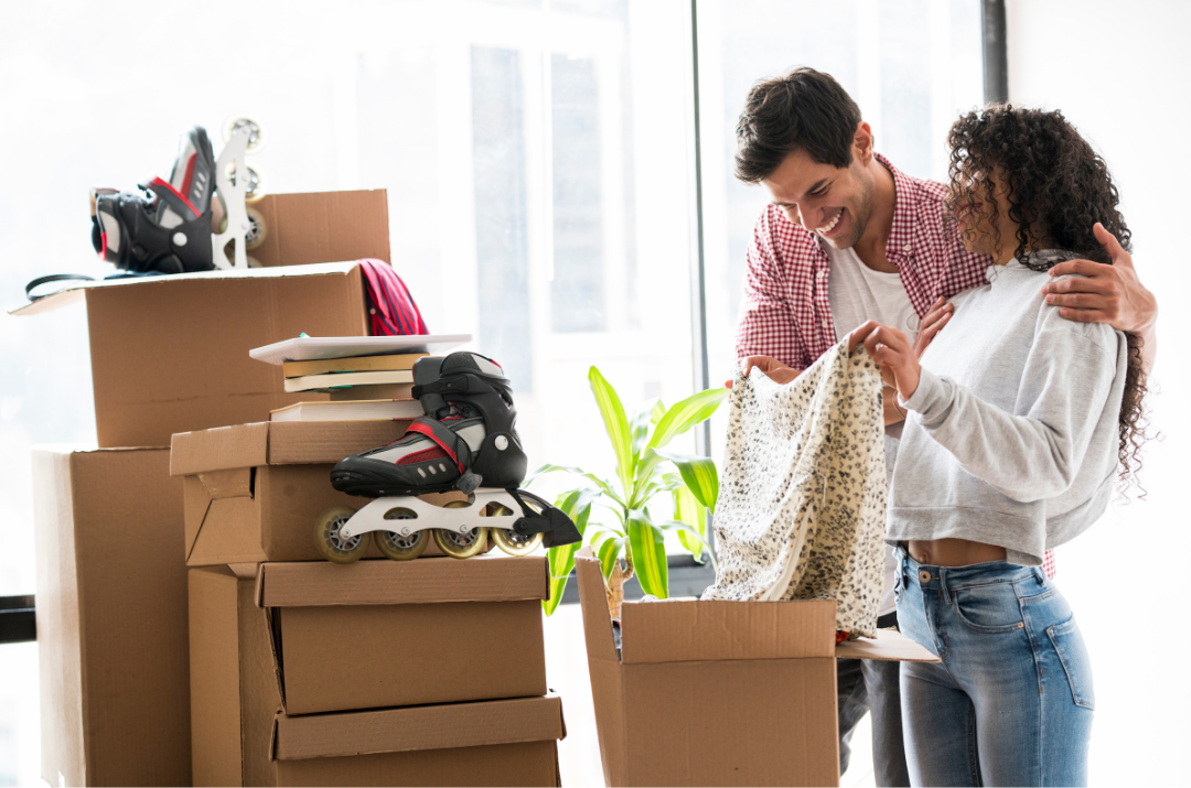 A couple packing clothes into a box surrounded by boxes.