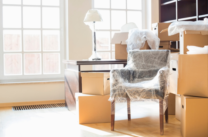 Furniture wrapped in plastic wrap surrounded by boxes.