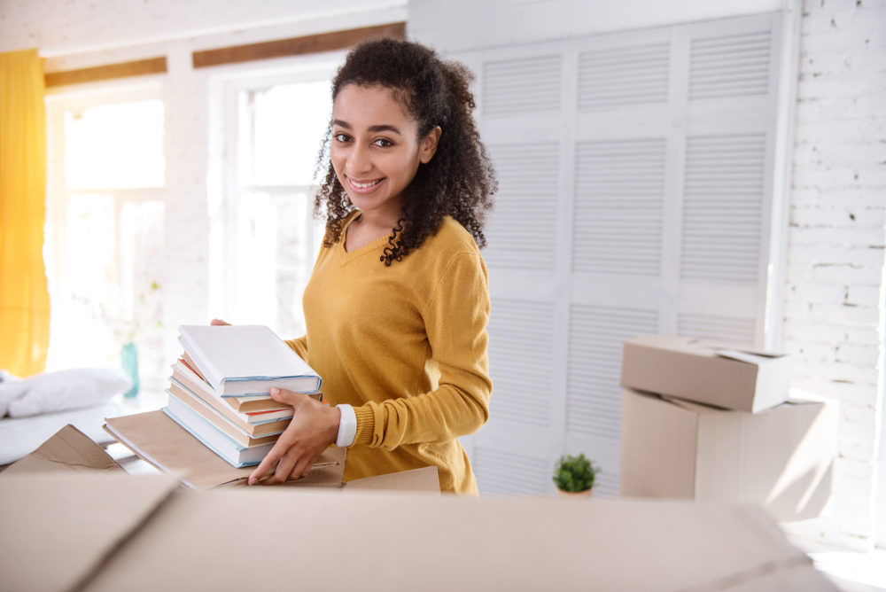 A woman packing books into a box surrounded by boxes.