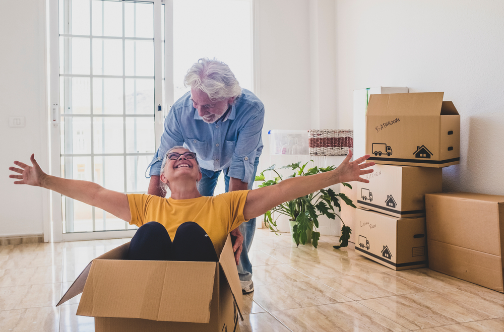 Older woman sitting in a box smiling with an older man.