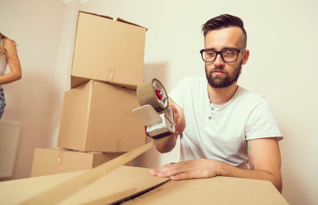 Man packing up boxes with tape surrounded by boxes.