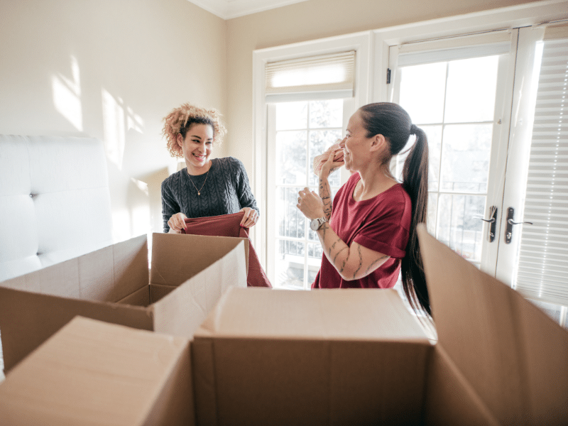 Two women packing clothes into boxes and smiling.