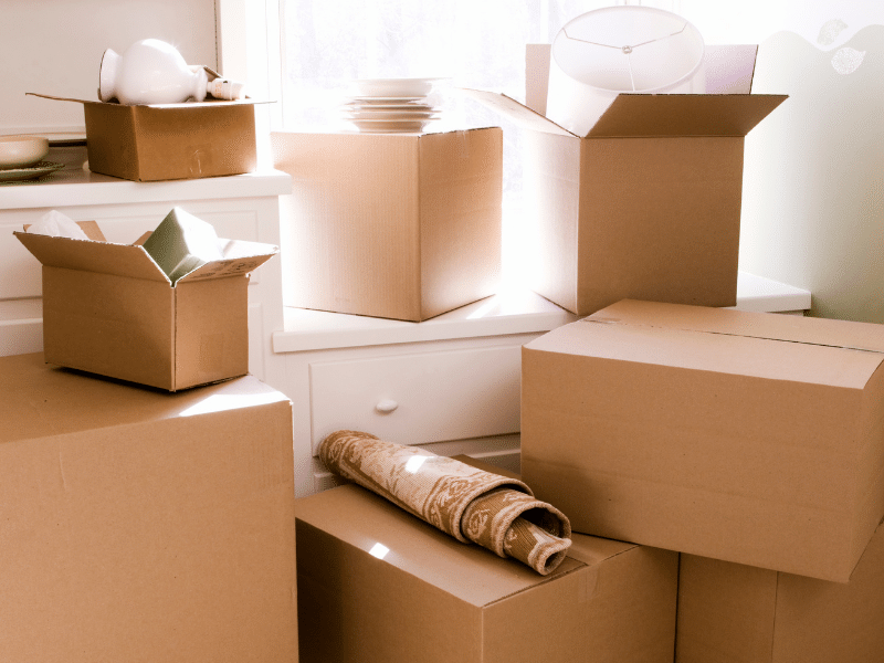 Cardboard moving boxes and a small rug sitting next to a window.