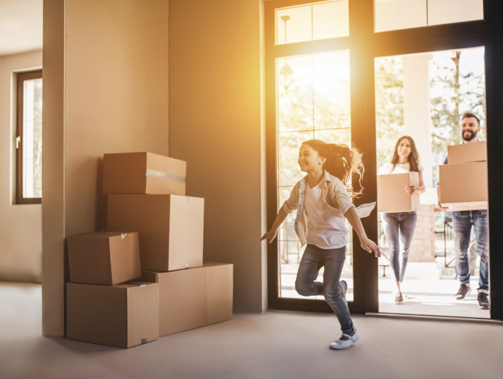 Young girl happily running into her new home as her parents carry cardboard boxes behind her.