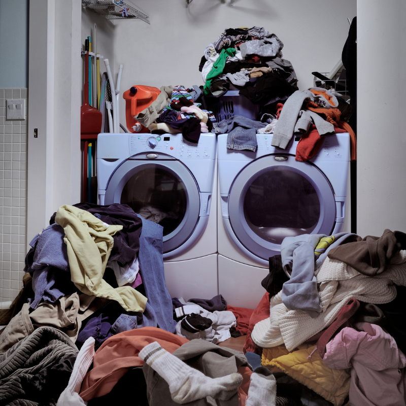 Washing and drying machine covered in clothes as clothes spill out from both machines.