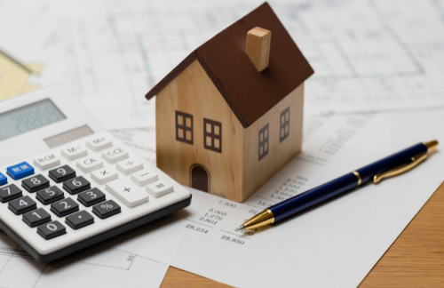 A toy house and a calculator laying on top of bills.