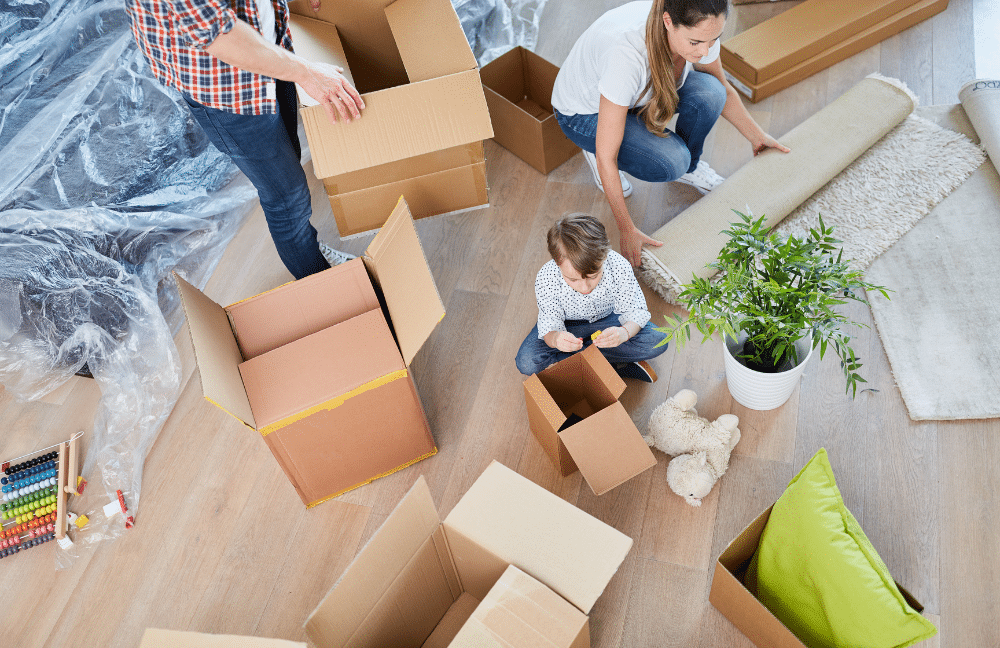 A family sitting on the ground unpacking boxes in their new house.