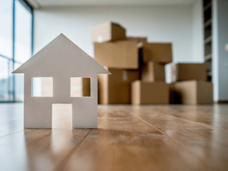 A piece of paper shaped like a house with a stack of boxes behind it