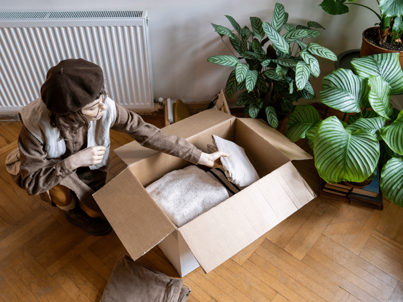 Someone packing clothes and towels into a cardboard box.