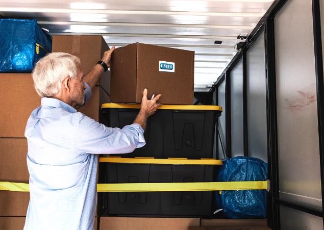 A man packing boxes with the units logo on them into a container.