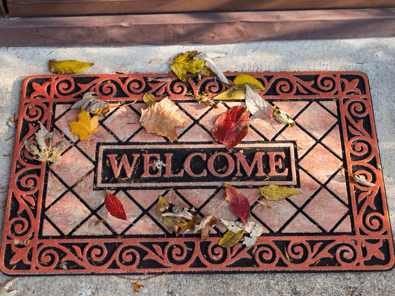 A welcome mat that is red and has leave on it.