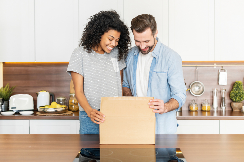 Couple smiling as they open a cardboard box.