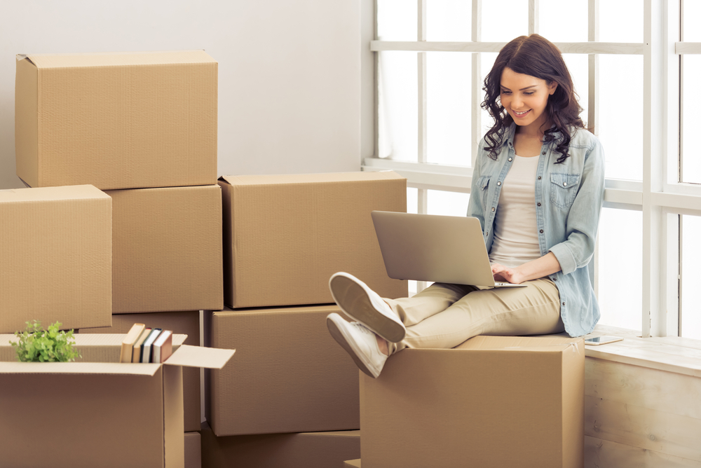 Woman sitting on a cardboard box working on her laptop.